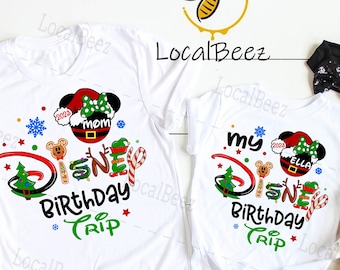 May include: Two white t-shirts with a Christmas-themed Disney birthday trip design. The adult shirt says "Disney Birthday Trip" with a Mickey Mouse wearing a Santa hat and the child's shirt says "My Disney Birthday Trip" with a Mickey Mouse wearing a Santa hat and the name "Ella".