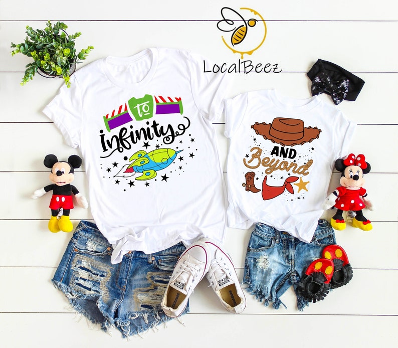 May include: Two white t-shirts with a Toy Story theme. The first shirt has a green rocket ship with the text "to infinity" and stars. The second shirt has a brown cowboy hat with the text "and beyond".