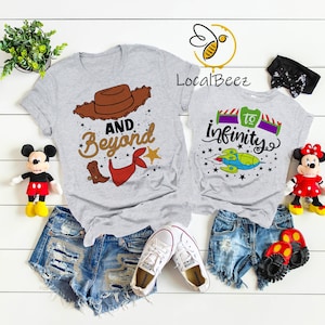 May include: Two gray t-shirts with a Toy Story theme. The larger shirt has a brown cowboy hat, red bandana, and the text "And Beyond". The smaller shirt has a cartoon spaceship and the text "To Infinity".