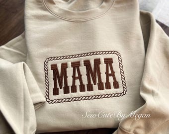 Könnte beinhalten: Ein beigefarbenes Sweatshirt mit Rundhalsausschnitt und einer braunen, gestickten rechteckigen Kordelumrandung. In der Mitte steht das Wort MAMA in großen braunen Blockbuchstaben. Der Text Sew Cute By Megan ist unten rechts zu sehen.
