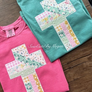 May include: Two crew neck sweatshirts, one pink and one teal, each featuring a patchwork cross design. The crosses are made of various floral and patterned fabrics. The text "Sew Cute By Megan" is visible.