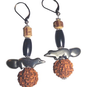 Puede incluir: Un par de pendientes de plata con una cuenta de madera marrón, una cuenta negra, un dije de animal de plata y una cuenta marrón.