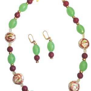 Peut inclure: Un collier vert et bordeaux avec des accents dorés et des perles à motifs floraux. Boucles d'oreilles assorties avec des perles vertes et bordeaux.