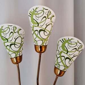 Könnte beinhalten: Eine dreiköpfige Messinglampe mit grün-weißen gemusterten Lampenschirmen. Die Lampenschirme haben ein wirbelndes Design.