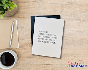May include: A white card with black text that reads "Don't cry because it's over, smile because you never have to see his mother again." The card is on a wooden surface with a black pen and a cup of coffee.