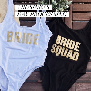 May include: Two one-piece swimsuits, one white and one black, with gold lettering. The white swimsuit says "BRIDE" and the black swimsuit says "BRIDE SQUAD". The image also includes the text "3 BUSINESS DAY PROCESSING".