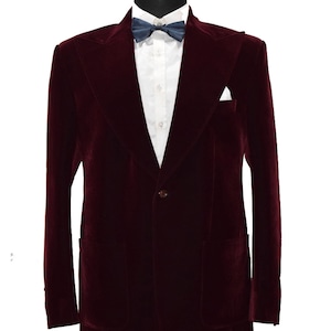 May include: A maroon velvet blazer with a single button fastening and a pocket on the left side. The blazer is on a mannequin wearing a white shirt and a dark blue bow tie.