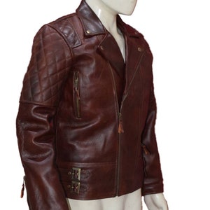 Puede incluir: Una chaqueta de cuero marrón con un diseño acolchado en los hombros y las mangas. La chaqueta tiene una cremallera y un cuello de pie.