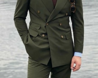 Puede incluir: Un traje de doble botonadura de color verde oscuro. El traje tiene un corte clásico y presenta una corbata marrón y unas gafas de sol.