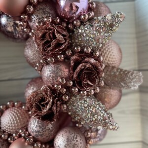 Peut inclure: Une couronne de No&euml;l rose et or rose avec des ornements, des perles et des fleurs.