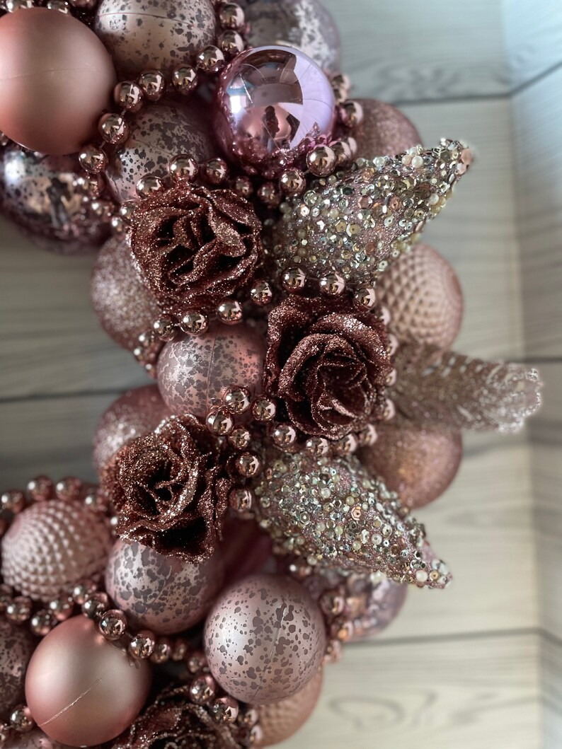 Peut inclure: Une couronne de No&euml;l rose et or rose avec des ornements, des perles et des fleurs.