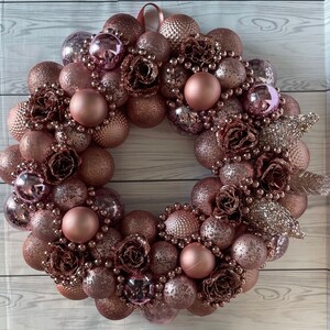 Peut inclure: Une couronne de No&euml;l rose gold d&eacute;cor&eacute;e d'ornements, de fausses fleurs et de paillettes. La couronne est faite de diff&eacute;rentes textures et tailles d'ornements.