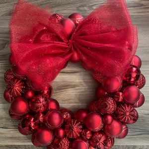 K&ouml;nnte beinhalten: Ein roter Weihnachtskranz aus roten Kugeln und einer roten T&uuml;llschleife.
