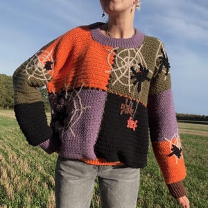 May include: A patchwork crochet sweater in orange, purple, black, and olive green. The sweater features spiderwebs and spiders. The sleeves are black and orange with brown cuffs. The sweater is worn over an orange shirt.