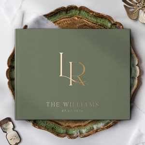 May include: A green wedding guest book with gold foil lettering. The book says "The Williams" and "07.12.2026". The book is on a decorative tray.