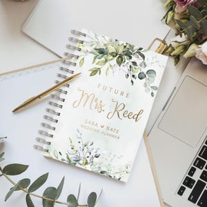 Personalized floral wedding planner book with gold foil text. Features elegant greenery artwork. Ideal for organizing wedding plans, budgeting, and checklists. A thoughtful bridal shower gift, engagement present, or keepsake for a bride-to-be.