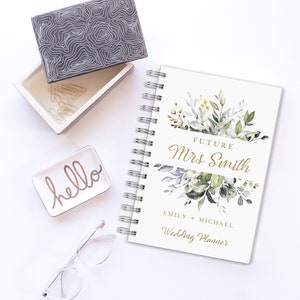 May include: A white wedding planner with a gold floral design and the text "Future Mrs. Smith Emily + Michael Wedding Planner".
