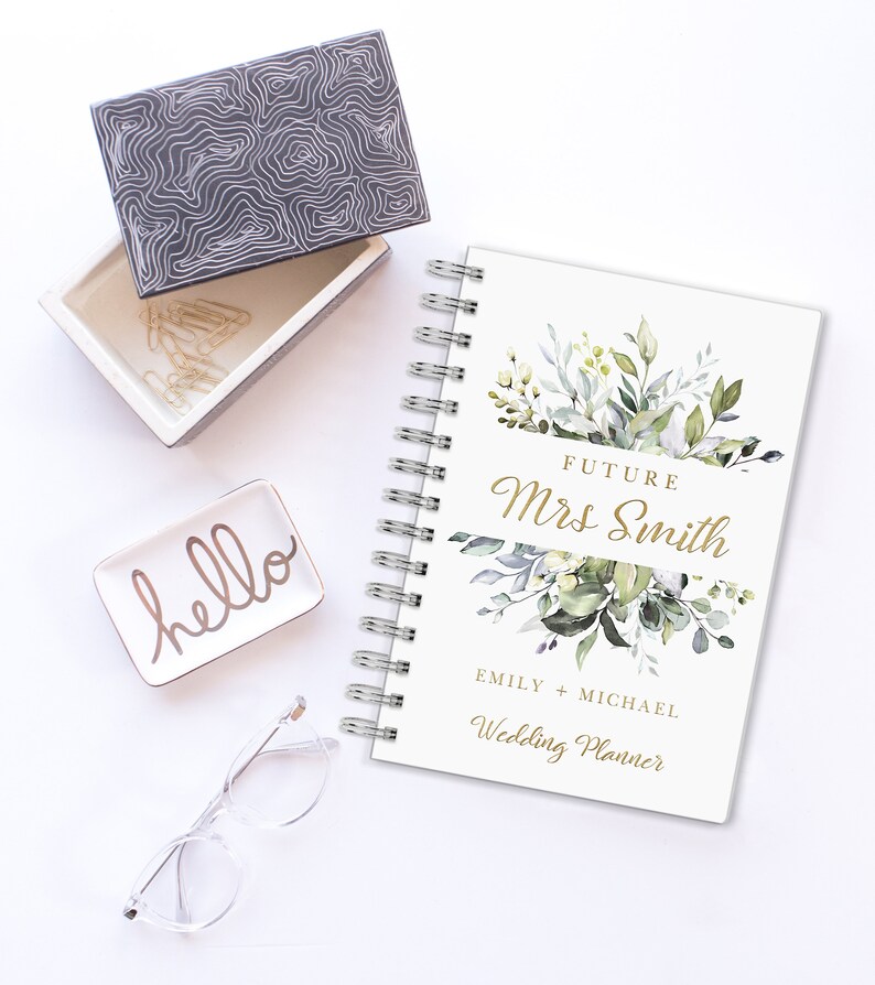 May include: A white wedding planner with a gold floral design and the text "Future Mrs. Smith Emily + Michael Wedding Planner".