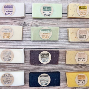 May include: Twelve bars of handmade tallow soap with various scents and ingredients. The soaps are arranged in three rows of four on a wooden surface. The scents include lavender peppermint, rosemary tea tree, lemon poppyseed, pure unscented, spearmint, oatmeal goats milk and honey, goats milk, coffee scrub, oatmeal goats milk and honey, pure unscented, charcoal tea tree and eucalyptus, and turmeric goats milk and honey.