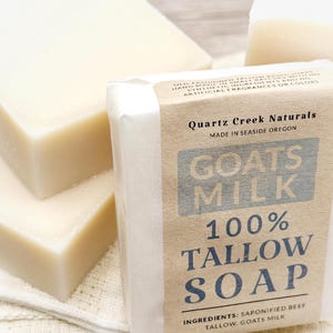 May include: Three rectangular bars of off-white soap. One bar is wrapped in a tan paper label that reads Quartz Creek Naturals, Made in Seaside Oregon, Goats Milk 100% Tallow Soap, and Ingredients: Saponified Beef Tallow, Goats Milk.