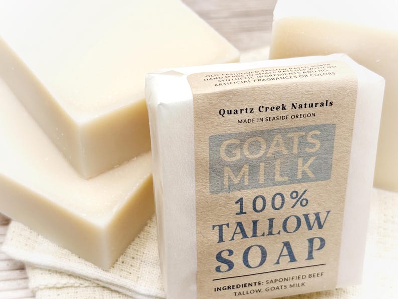 May include: Three rectangular bars of off-white soap. One bar is wrapped in a tan paper label that reads Quartz Creek Naturals, Made in Seaside Oregon, Goats Milk 100% Tallow Soap, and Ingredients: Saponified Beef Tallow, Goats Milk.