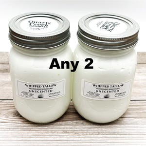 May include: Two 16-ounce glass jars filled with white whipped tallow cream. The jars have silver lids with labels that read "Quartz Creek Naturals" and "Whipped Tallow Nourishing Skin Cream Unscented". The jars are on a wooden surface. Any 2.