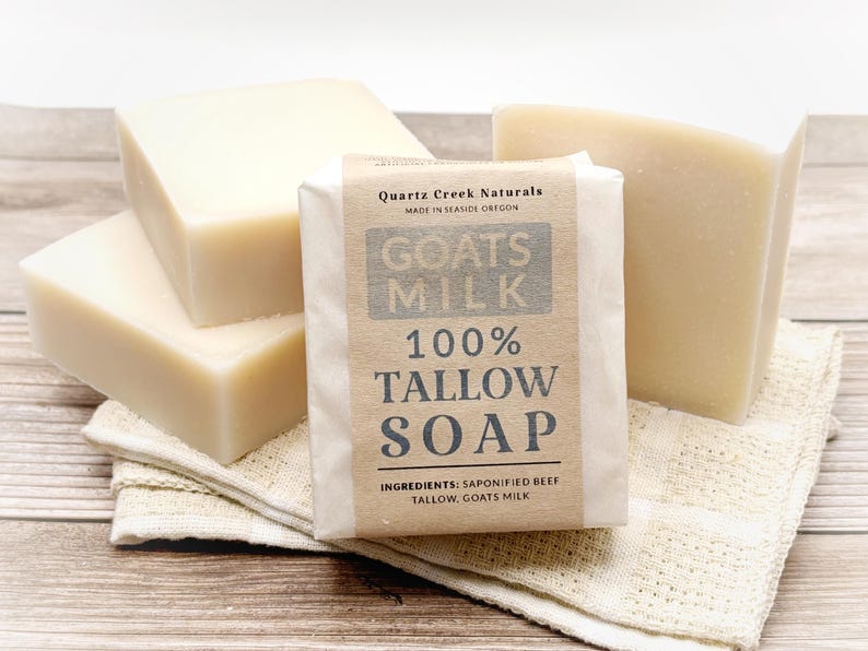 May include: Four rectangular bars of off-white soap. One bar is wrapped in a tan paper label with black text reading Quartz Creek Naturals, Goats Milk, 100% Tallow Soap, and Ingredients: Saponified Beef Tallow, Goats Milk. The soap is stacked.