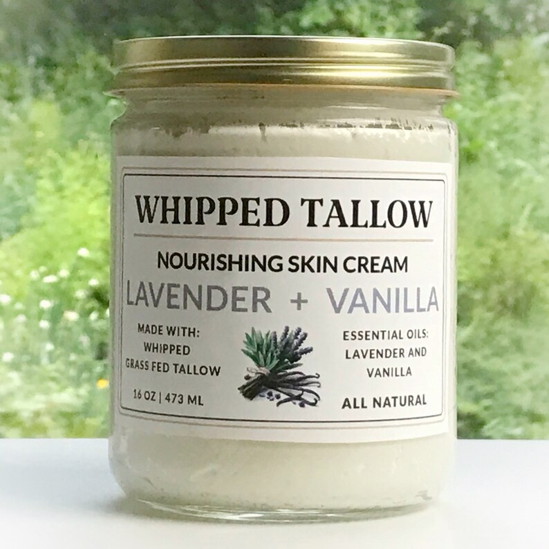 May include: A glass jar with a gold lid containing a white whipped cream. The label reads "Whipped Tallow Nourishing Skin Cream Lavender + Vanilla Made with: Whipped Grass Fed Tallow 16 oz | 473 ml Essential Oils: Lavender and Vanilla All Natural".