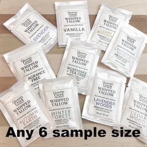May include: A collection of ten small, white, sample-sized pouches of whipped tallow skin cream. Each pouch features a different scent, including Lavender, Vanilla, Cedar + Bergamot, Lavender + Vanilla, Rosemary + Tea Tree, Winter Forest, Autumn Earth, and Lavender Woods. The pouches are arranged in a grid pattern on a wooden surface. The text "Any 6 sample size" is printed below the pouches.