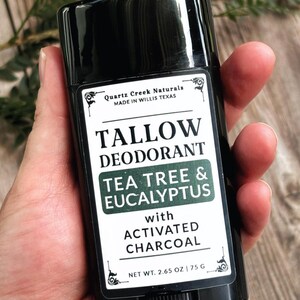 K&ouml;nnte beinhalten: Ein schwarzer, zylindrischer Deodorant-Stick mit einem wei&szlig;en Etikett. Das Etikett tr&auml;gt die Aufschrift Quartz Creek Naturals, Tallow Deodorant, Tea Tree & Eucalyptus with Activated Charcoal und Net Wt. 2.65 oz | 75 g. Der Text ist schwarz und gr&uuml;n.