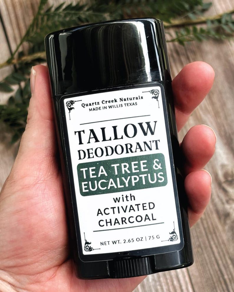 K&ouml;nnte beinhalten: Ein schwarzer, zylindrischer Deodorant-Stick mit einem wei&szlig;en Etikett. Das Etikett tr&auml;gt die Aufschrift Quartz Creek Naturals, Tallow Deodorant, Tea Tree & Eucalyptus with Activated Charcoal und Net Wt. 2.65 oz | 75 g. Der Text ist schwarz und gr&uuml;n.