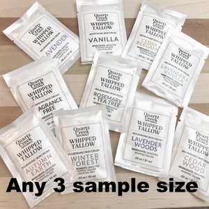 May include: A collection of eight small white pouches with labels for different scented whipped tallow skin creams. The labels feature the brand name "Quartz Creek Naturals" and the scent names, such as "Lavender", "Vanilla", "Cedar + Bergamot", "Rosemary + Tea Tree", "Winter Forest", "Lavender Woods", and "Autumn Earth". The pouches are arranged on a wooden surface. The text "Any 3 sample size" is visible at the bottom of the image.