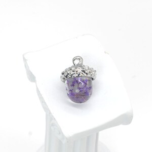 May include: A silver acorn charm with a clear glass top filled with dried purple flowers.