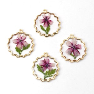 May include: Four gold-toned charms with a scalloped edge, each featuring a pressed pink and white flower with green leaves encased in clear resin.