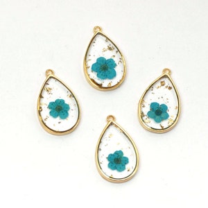 May include: Four gold teardrop-shaped pendants with clear resin and a single blue flower pressed inside each. The resin is filled with gold flecks.