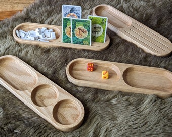May include: Wooden game organizers in various shapes, including oval trays with compartments and slots for cards. The organizers hold game pieces, dice, and cards. The wood has a natural, light brown color, and the background is a brown, furry surface.
