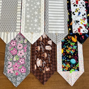 May include: Six different table runners with various patterns. The runners are all gray, white, and black with different designs. The designs include stars, stripes, coffee cups, flowers, and Mickey Mouse characters.
