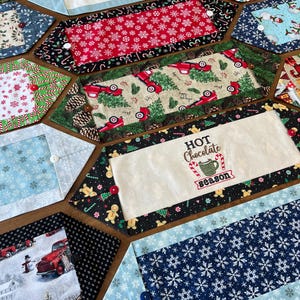 May include: A collection of festive, handmade Christmas table runners. Designs include snowflakes, red trucks, snowmen, and the text "Winter Wonderland" and "Hot Chocolate Season". Each runner is a unique shape and features a button detail.