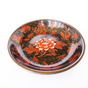 May include: A black and gold ceramic dish with a red and white floral design. The dish has a glossy finish and is decorated with a delicate floral pattern.