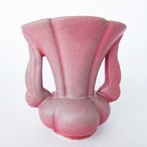 May include: A pink ceramic vase with two handles. The vase has a rounded bottom and a flared top.