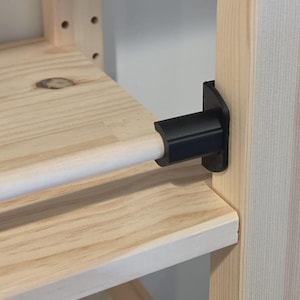 May include: Close-up of a wooden shelf with a black bracket holding a wooden dowel. The shelf is made of light-colored wood, and the bracket is attached to a vertical support.