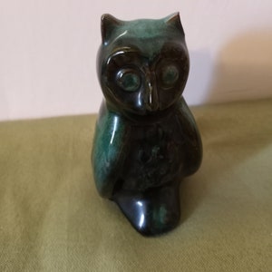 May include: A ceramic owl figurine with a dark green and black glaze. The owl is sitting with its wings folded and has a round head with large eyes.