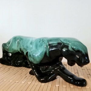 May include: A ceramic panther figurine in a black and green glaze. The panther is in a crouching position with its head lowered.