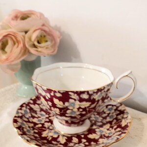 May include: A burgundy teacup and saucer with a floral pattern. The cup and saucer have a gold trim.