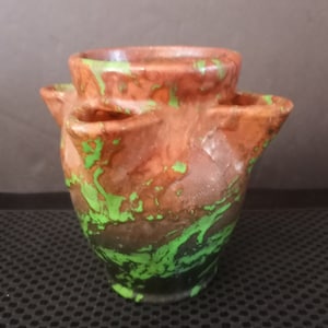 May include: A terracotta planter with a green and brown marbled glaze. The planter has four openings around the top, making it ideal for planting multiple small plants.
