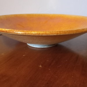 May include: A large, round, orange ceramic bowl with a white glaze on the bottom. The bowl is sitting on a wooden surface.