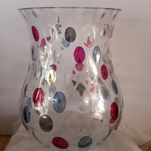 May include: A clear glass vase with a textured surface and a polka dot pattern in shades of pink, blue, and grey. The vase has a wide mouth and a narrow base.