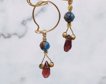 May include: A pair of gold hoop earrings with dangling charms. Each charm features a blue and red gemstone, with a smaller gold bead in between.