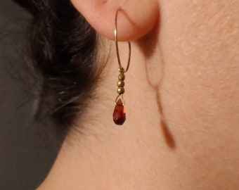 May include: Gold hoop earrings with a dangling red teardrop crystal and gold beads.