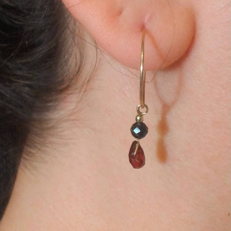 May include: Gold hoop earrings with a black bead and a red gemstone dangle.